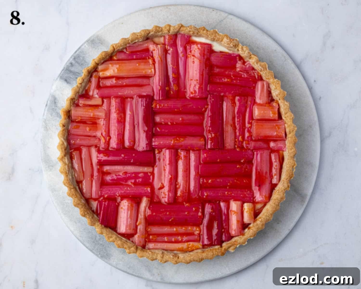 The fully assembled vegan rhubarb tart, with vibrant roasted rhubarb pieces artistically arranged over the creamy vanilla filling.