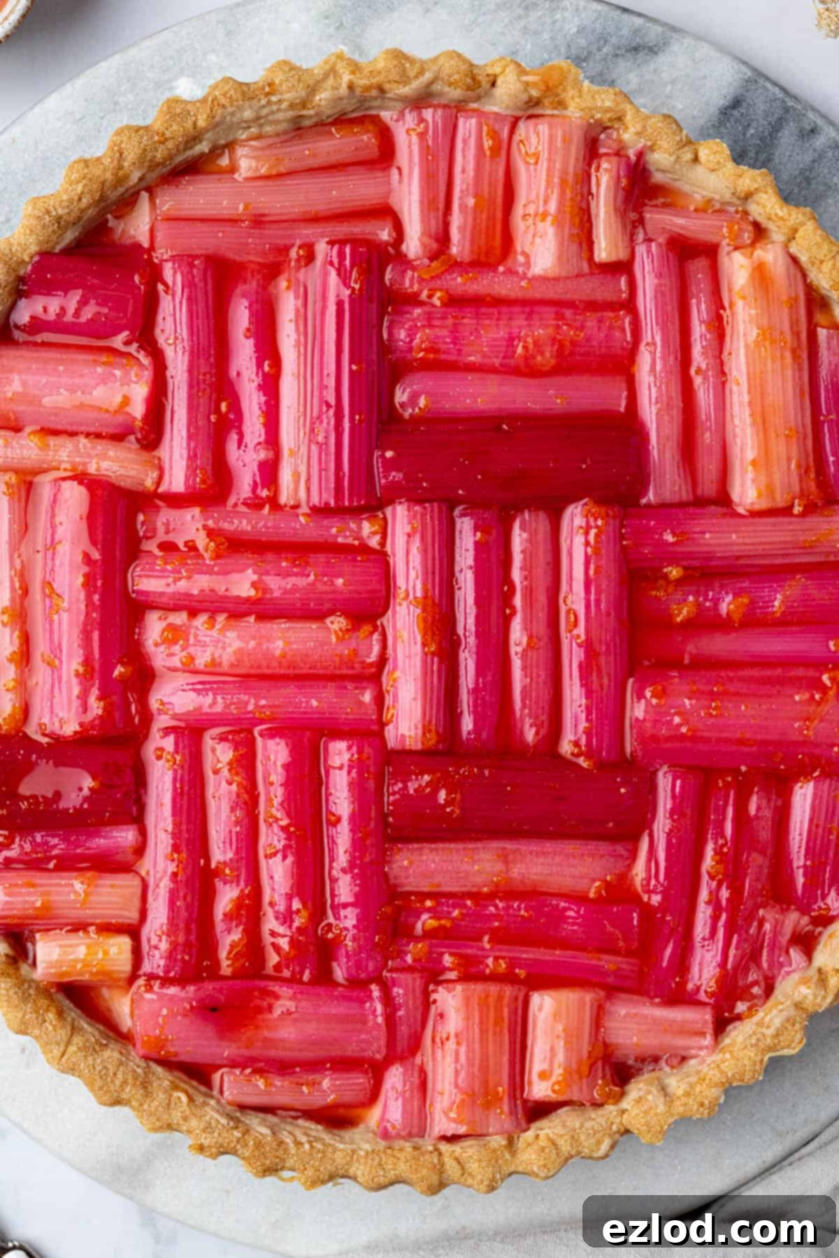 A close-up of a beautifully presented slice of vegan rhubarb tart, showcasing the crisp pastry, creamy vanilla filling, and vibrant roasted rhubarb on top.