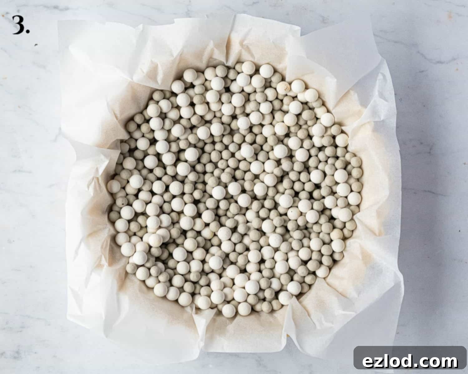 A tart shell lined with baking parchment and filled with baking beans, prepared for blind baking.