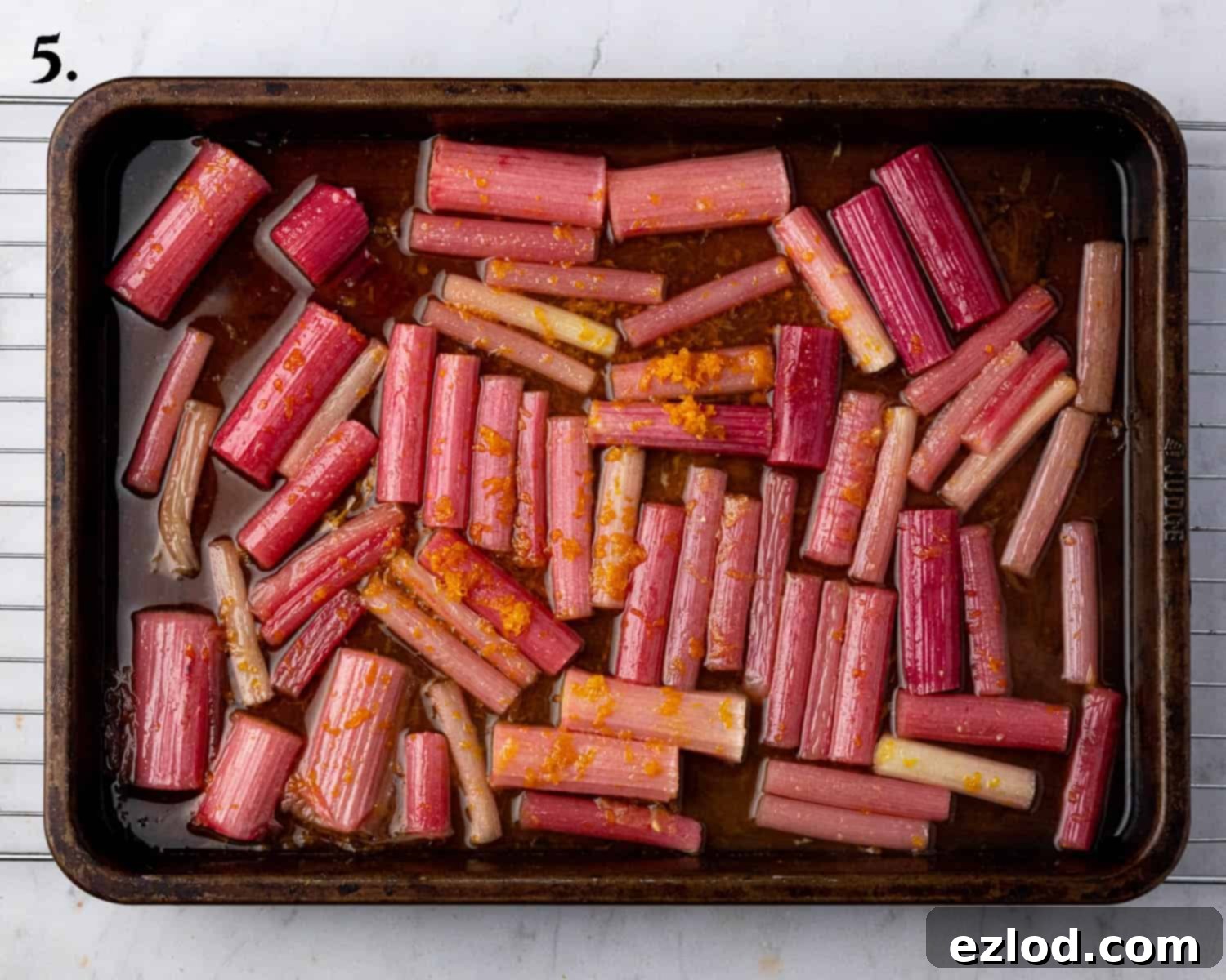 Fresh rhubarb pieces arranged in a single layer in a roasting tin, seasoned with sugar, orange zest, orange juice, and vanilla, ready for roasting.