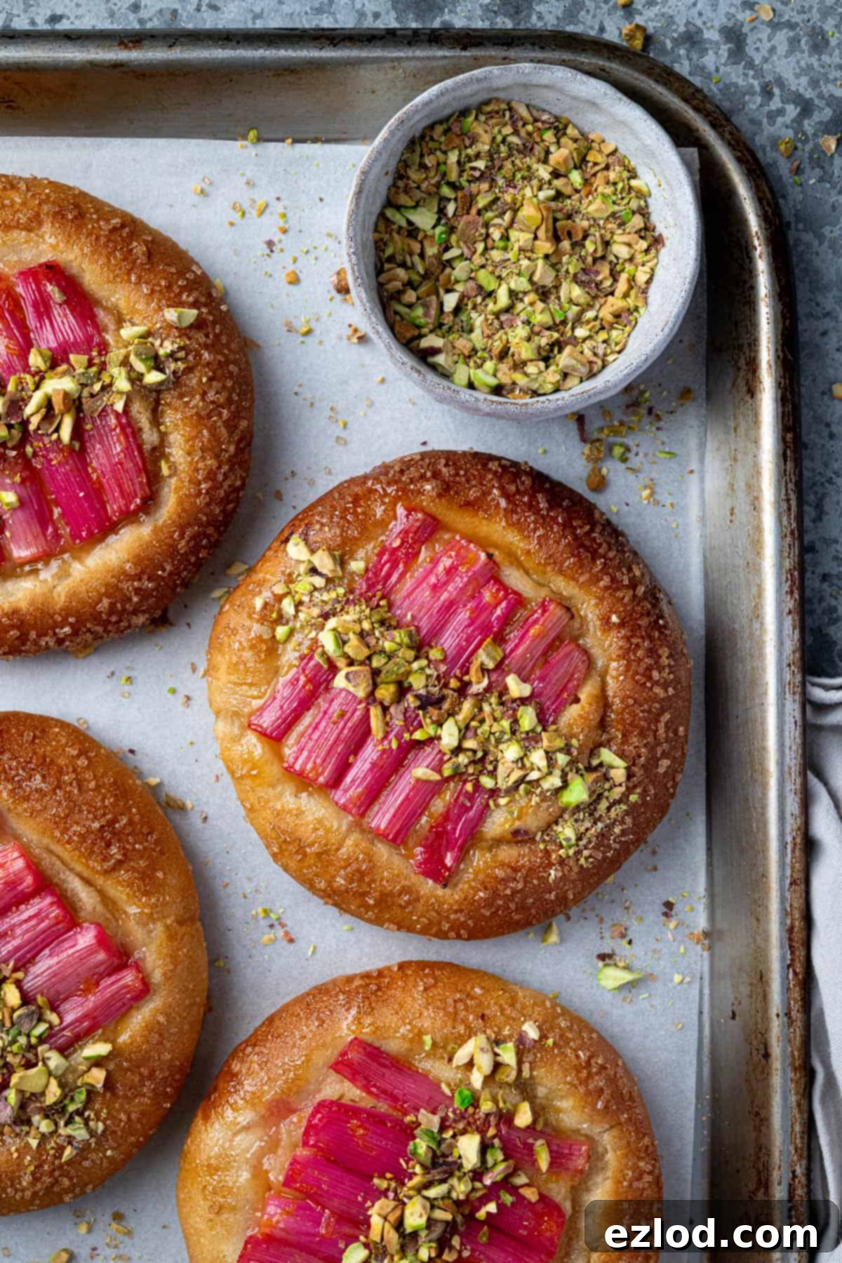 Freshly baked vegan rhubarb frangipane buns on a baking tray, garnished with a sprinkle of chopped pistachios.