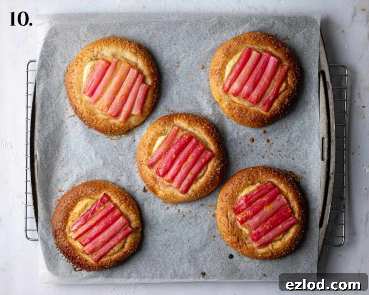 Step 10: Freshly baked vegan rhubarb frangipane buns, golden brown and perfectly risen, cooling on a baking sheet.