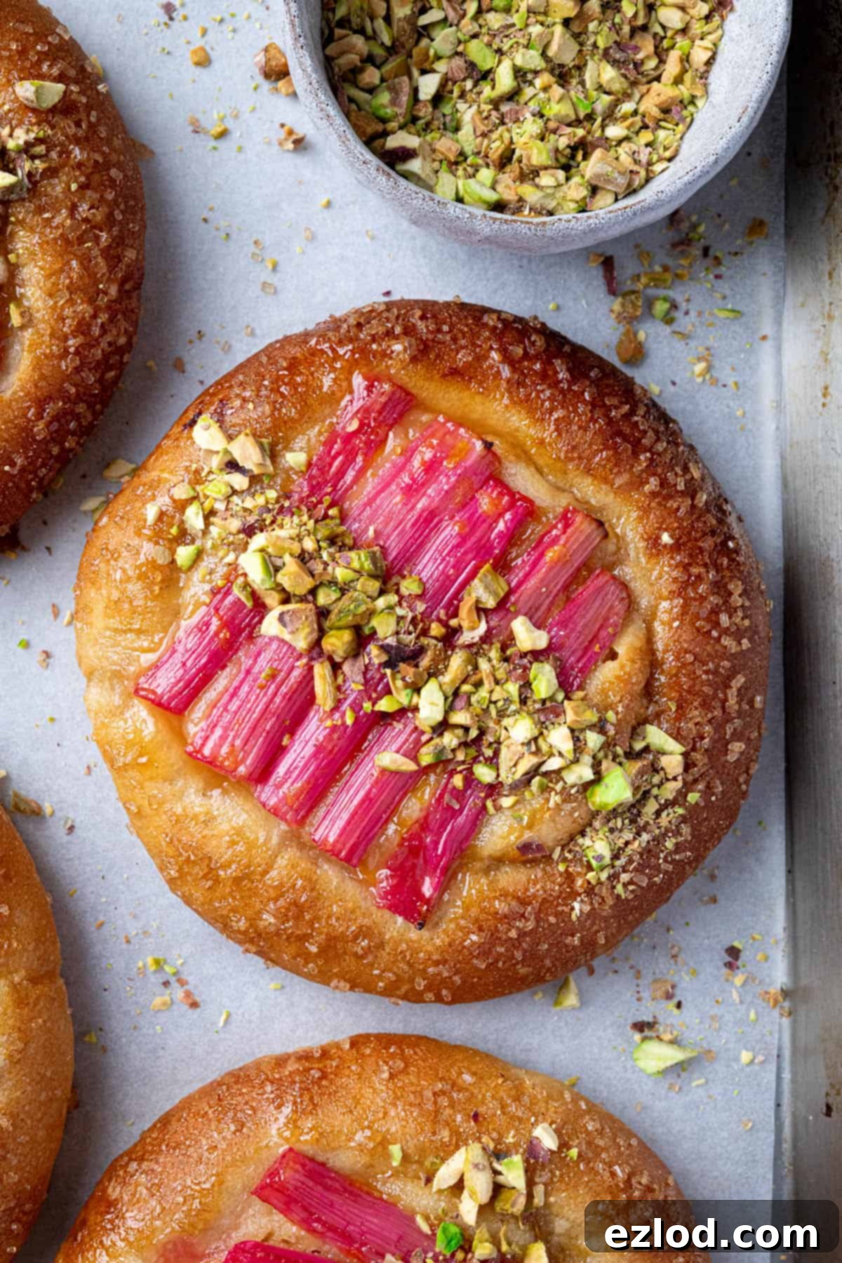 A close-up shot of a single vegan rhubarb frangipane bun, highlighting its textures and vibrant colors.