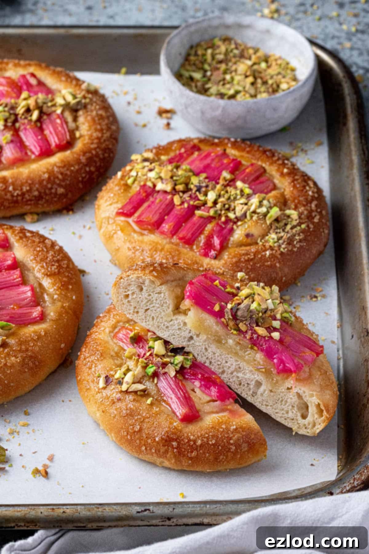 A baking sheet displaying several vegan rhubarb frangipane buns, with one bun sliced in half to show its interior.