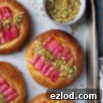 Freshly baked vegan rhubarb frangipane buns on a baking tray, garnished with a sprinkle of chopped pistachios.