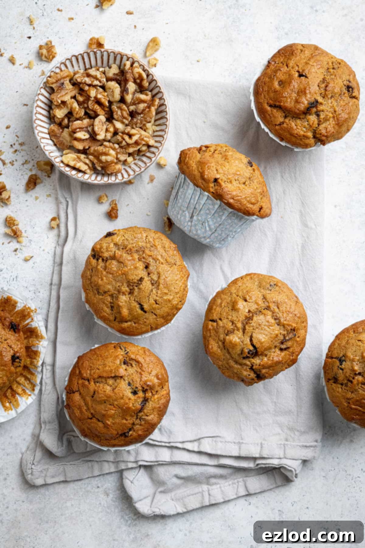 Perfectly Moist Vegan Carrot Muffins 11 Vegan carrot muffins on a tea towel with a bowl of walnuts.