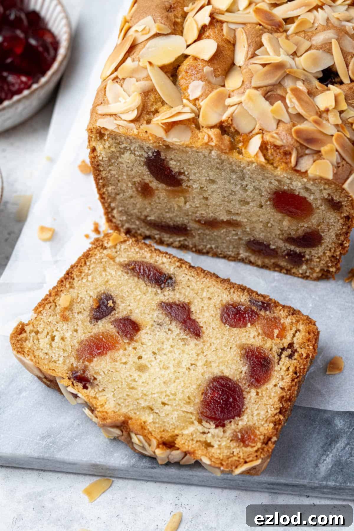 A beautiful close-up of a single slice of vegan cherry almond loaf cake, highlighting its delicate texture and the appealing distribution of glacé cherries within.