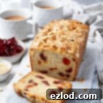 The delicious Vegan Cherry Loaf Cake presented on a marble board, accompanied by tea and bowls of glacé cherries and flaked almonds.