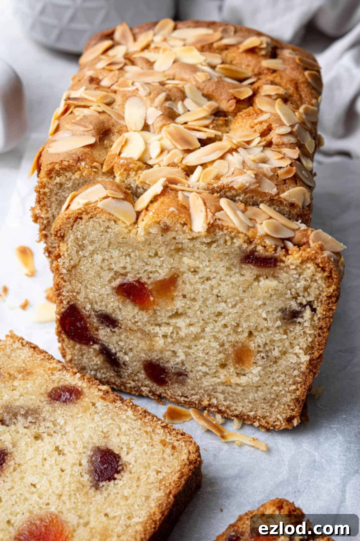 A close-up view of a perfectly sliced vegan cherry loaf cake, showcasing its moist, tender crumb and the generous distribution of vibrant glacé cherries and almond flakes throughout.