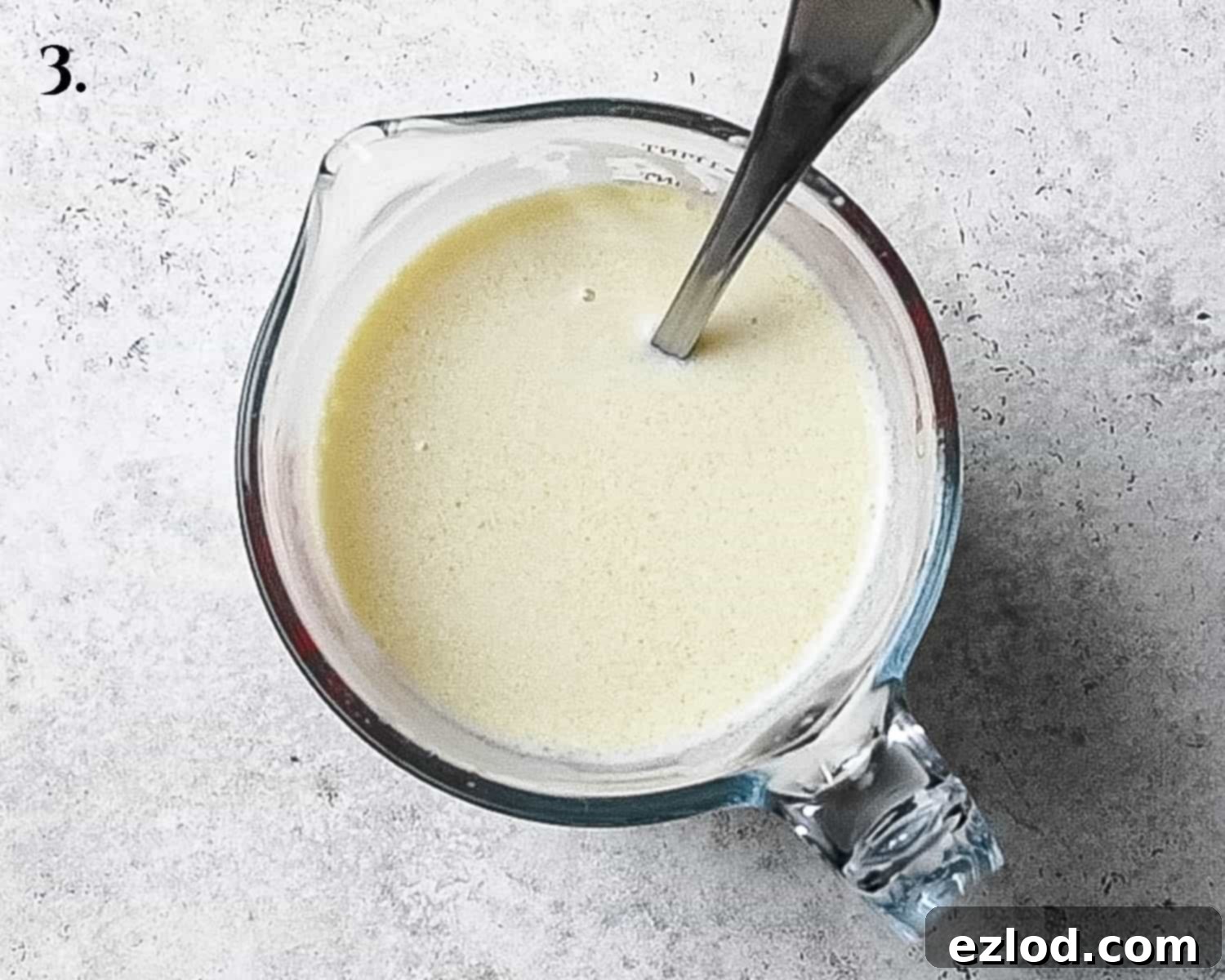 A clear jug holding the meticulously whisked wet ingredients: non-dairy milk, yogurt, oil, lemon juice, and both vanilla and almond extracts, creating a smooth, uniform mixture.