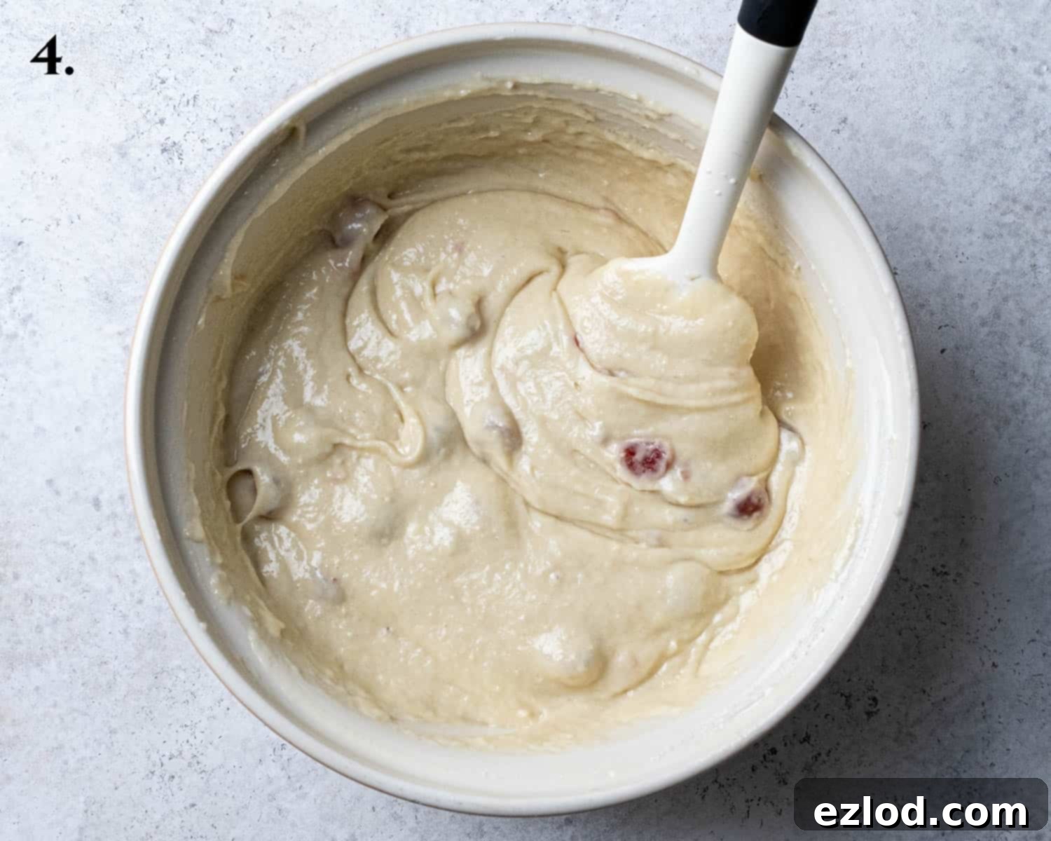 The perfectly mixed cake batter, showing its smooth consistency with a few minor lumps, and the initial incorporation of the prepared glacé cherries, ready for baking.