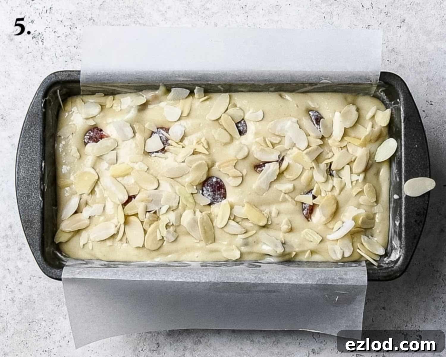 The vegan cherry loaf cake batter, now smoothed into a greased and lined loaf tin, topped with the remaining glacé cherries gently pressed in and a sprinkle of flaked almonds, poised for baking.