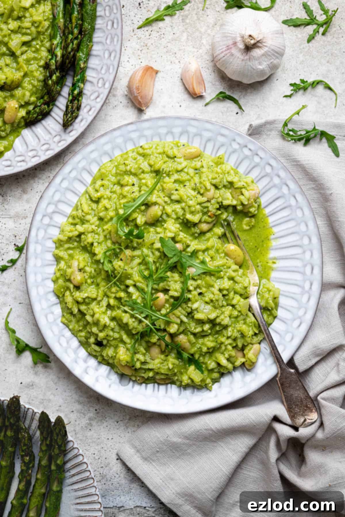 A plate of rocket pesto risotto with grilled asparagus, garnished with fresh herbs and a lemon wedge.
