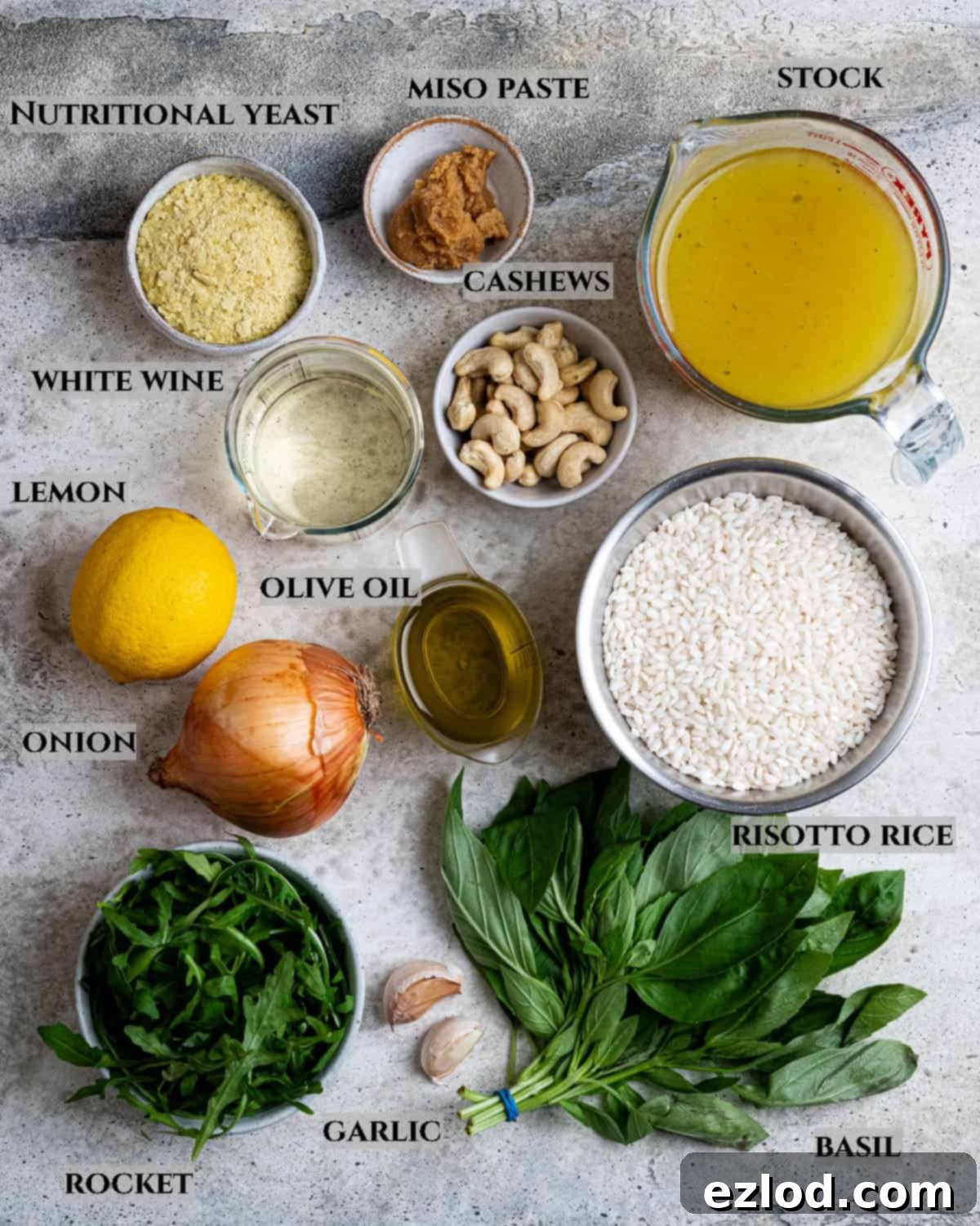 A labeled photo displaying all the fresh and pantry ingredients required to prepare the vegan rocket pesto risotto.