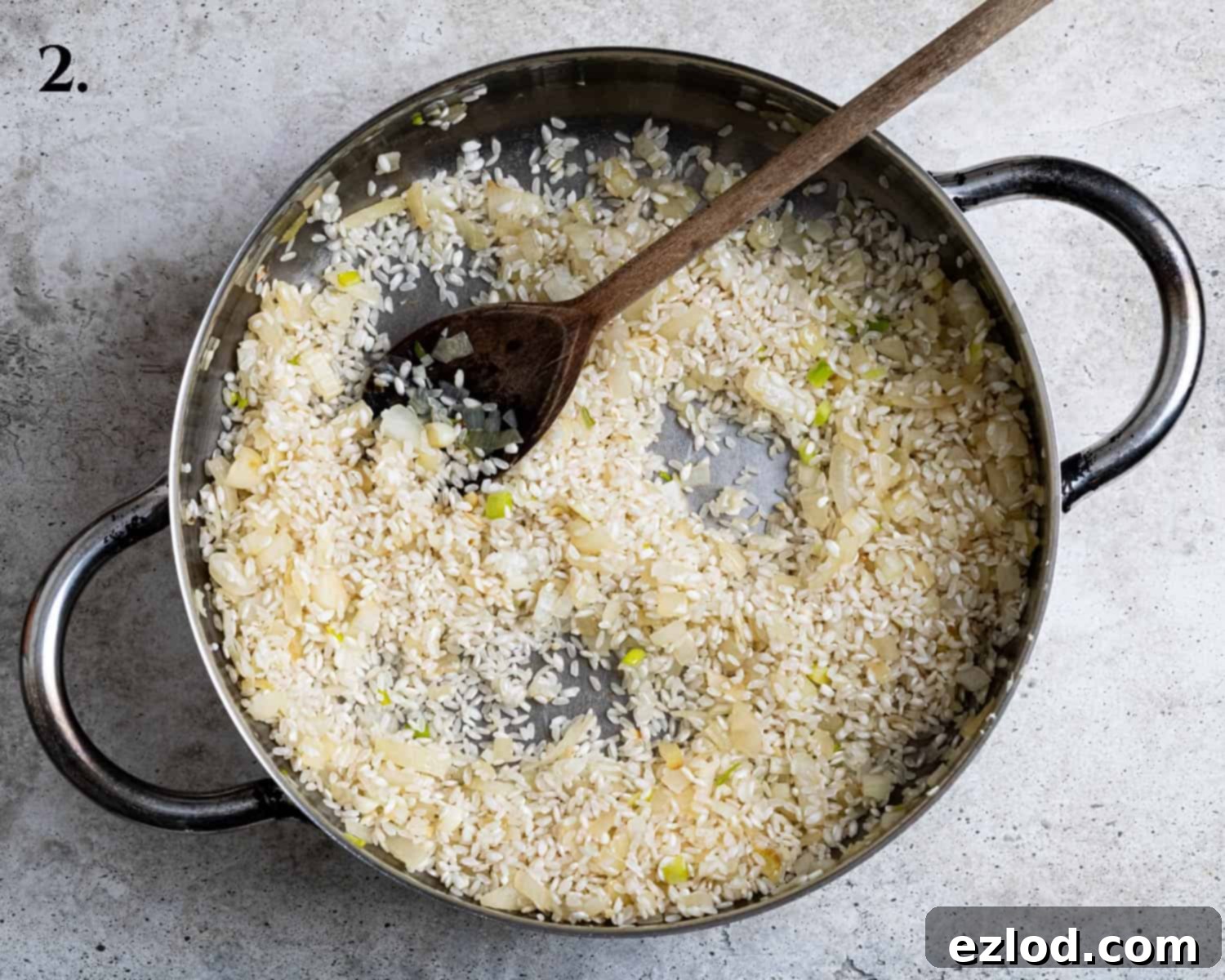 Step 2: Finely chopped onions and risotto rice being sautéed in a large pan, forming the aromatic base of the risotto.