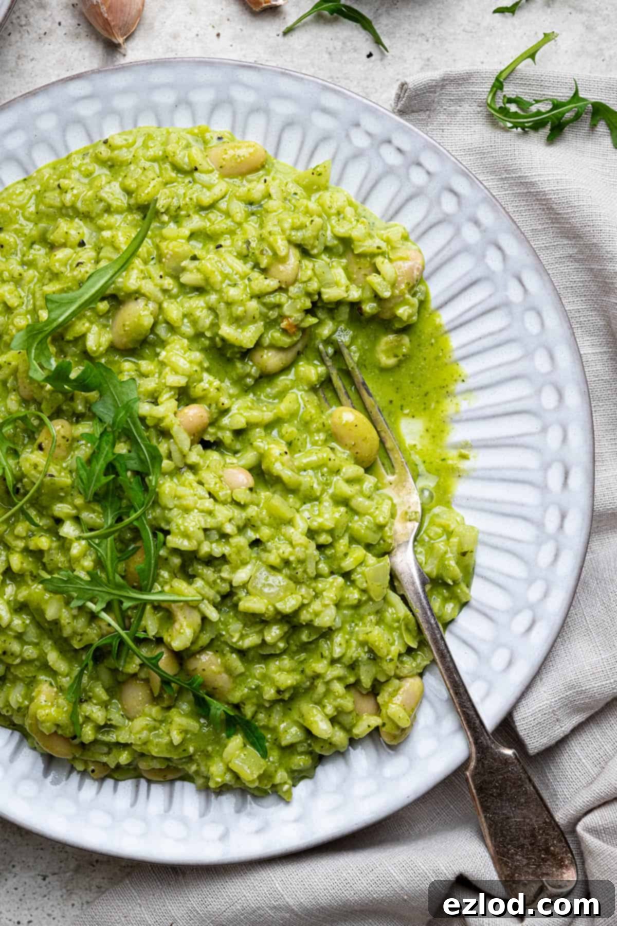 A close-up of a plate of vibrant green rocket pesto risotto, garnished with fresh rocket leaves and a touch of black pepper, ready to be enjoyed.