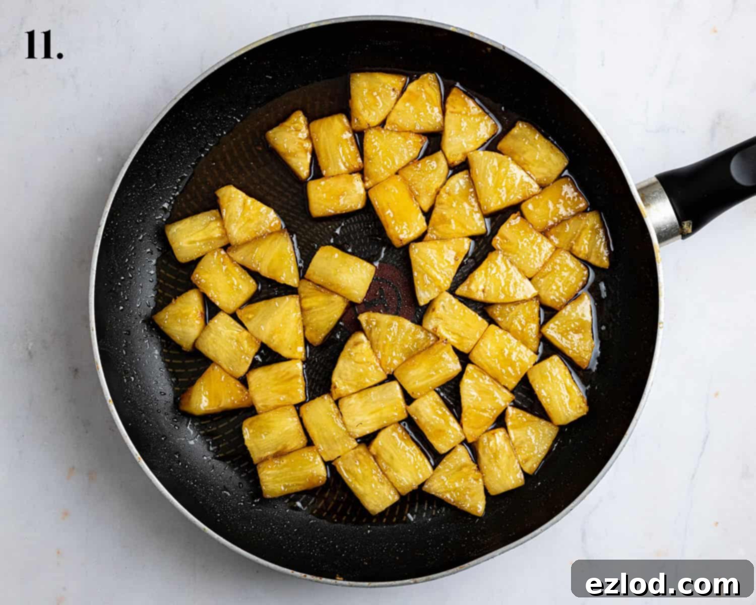 Caramelised pineapple chunks glistening in a sticky, reduced syrup in the frying pan after the reserved sugar liquid has been cooked down.