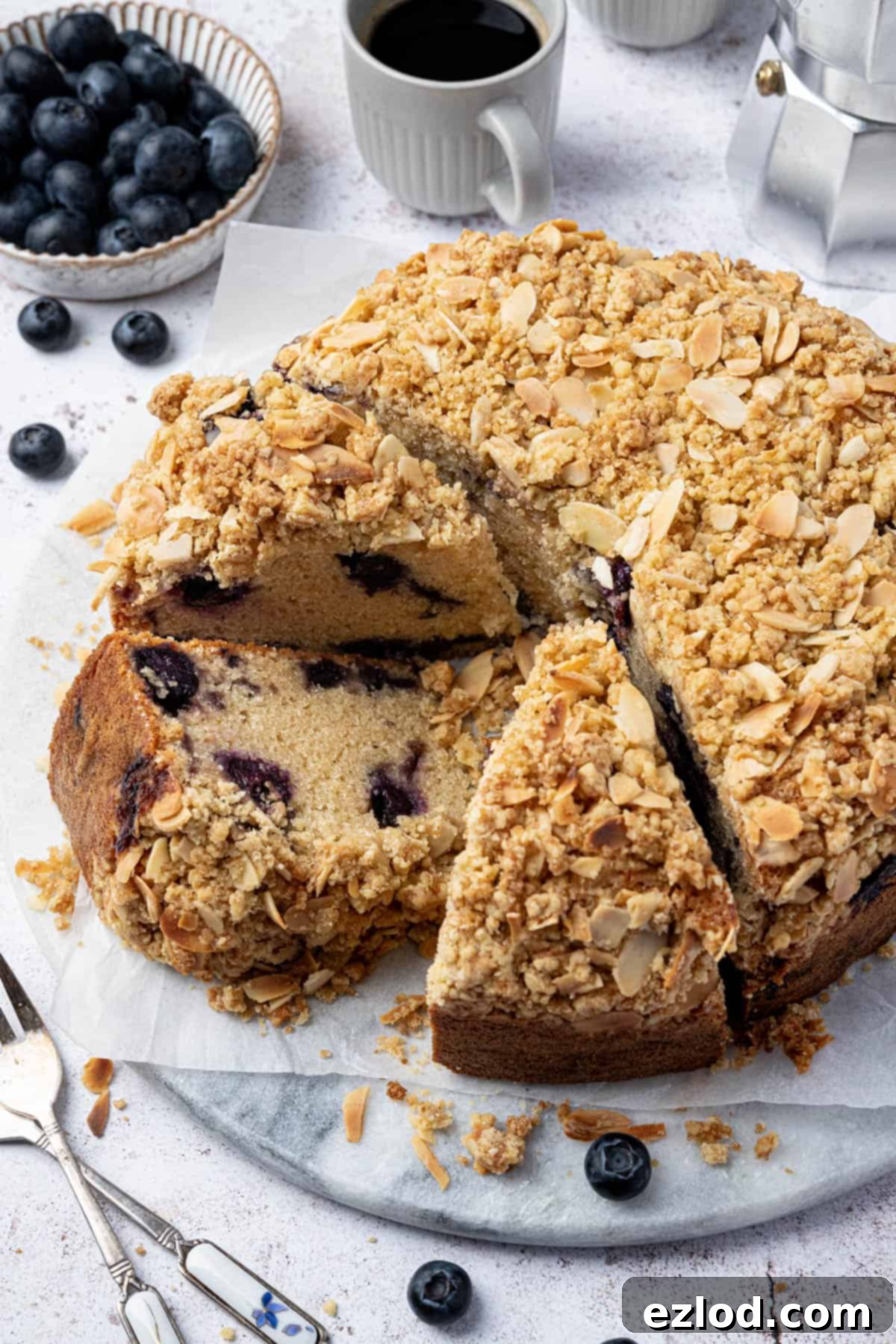 A large, beautifully sliced vegan blueberry crumb cake presented on a marble plate, showing its inviting texture and luscious blueberries.