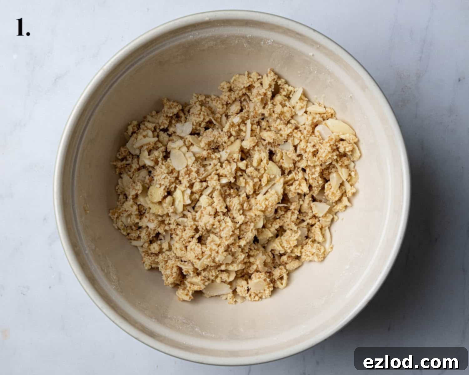 Step 1: The prepared streusel topping, a crumbly mix of flour, vegan butter, sugar, and flaked almonds, resting in a bowl.