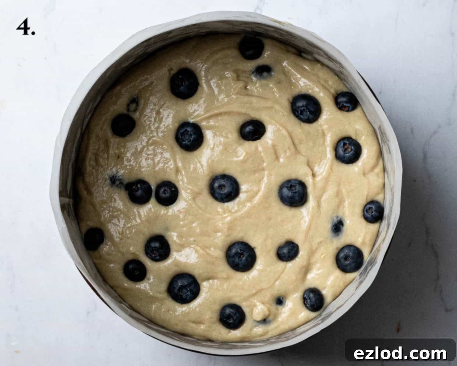 Step 4: The cake batter poured into a lined cake tin, with fresh blueberries scattered over the top, ready for the streusel.