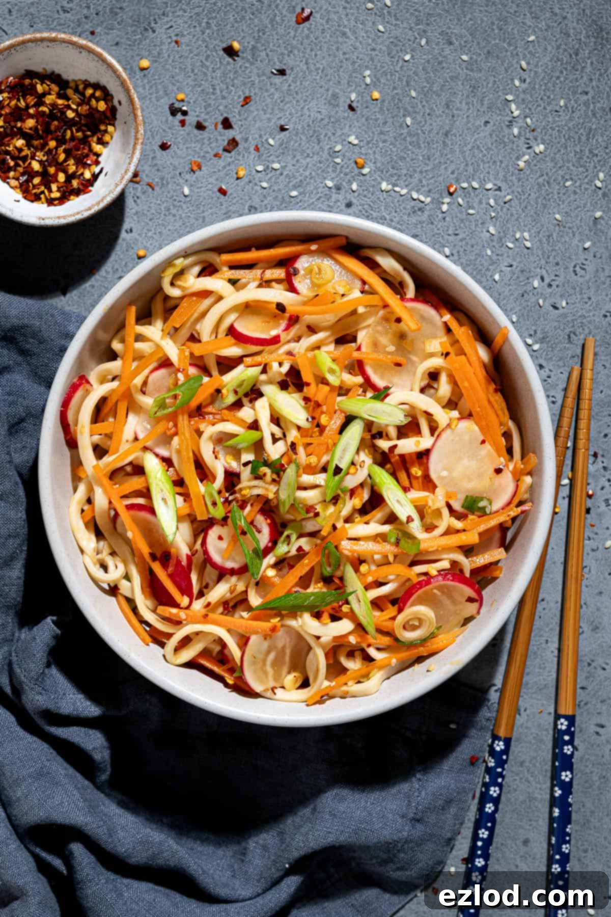 A bowl of vegan noodle salad with chopsticks and a bowl of chilli flakes.