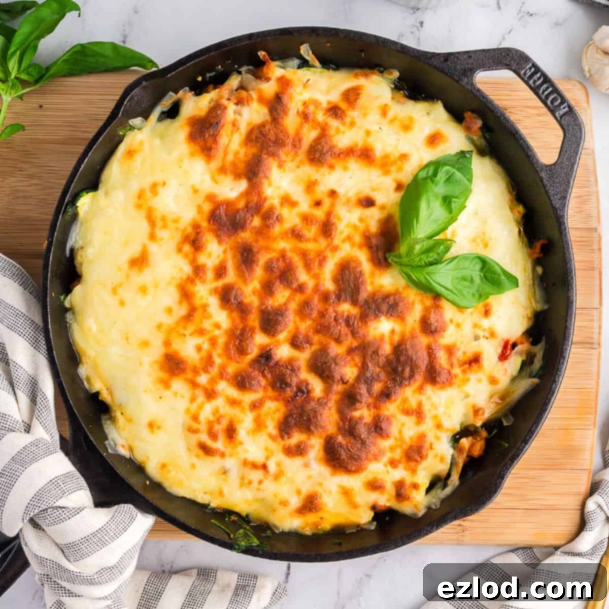 High Protein One Pan Zucchini Lasagna 2 A cast iron skillet filled with freshly baked zucchini lasagna, richly topped with golden-brown, bubbling cheese and garnished with fresh basil leaves. The skillet sits on a rustic wooden surface, surrounded by elegant plates, cutlery, and a small bowl of grated Parmesan cheese, hinting at a ready-to-serve meal.