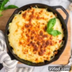 High Protein One Pan Zucchini Lasagna 9 A cast iron skillet filled with freshly baked zucchini lasagna, richly topped with golden-brown, bubbling cheese and garnished with fresh basil leaves. The skillet sits on a rustic wooden surface, hinting at a ready-to-serve meal.