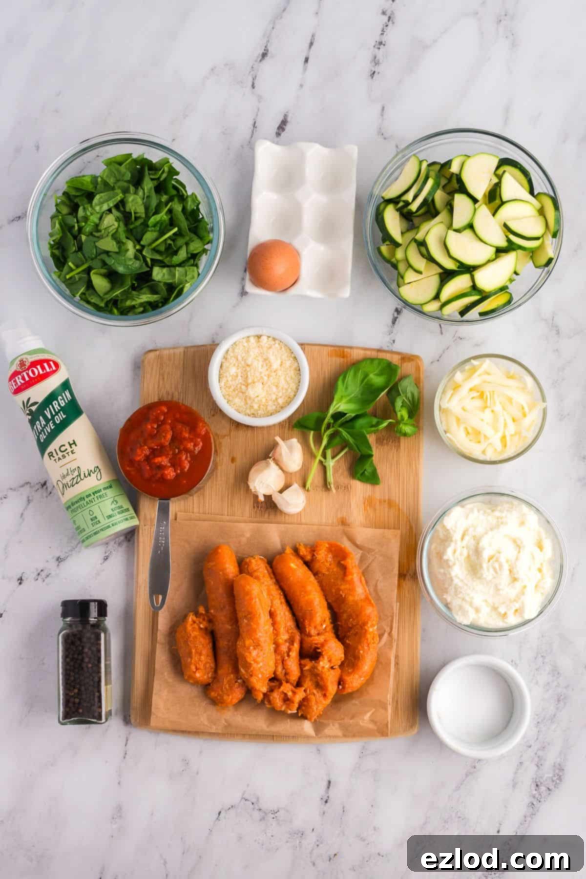 High Protein One Pan Zucchini Lasagna 4 A vibrant flat lay of all ingredients for zucchini lasagna artfully arranged on a marble countertop, including fresh spinach, sliced zucchini, an egg, creamy ricotta, shredded mozzarella, rich tomato sauce, grated Parmesan, minced garlic, lean Italian sausage, fresh basil, a bottle of olive oil spray, and a pepper grinder.