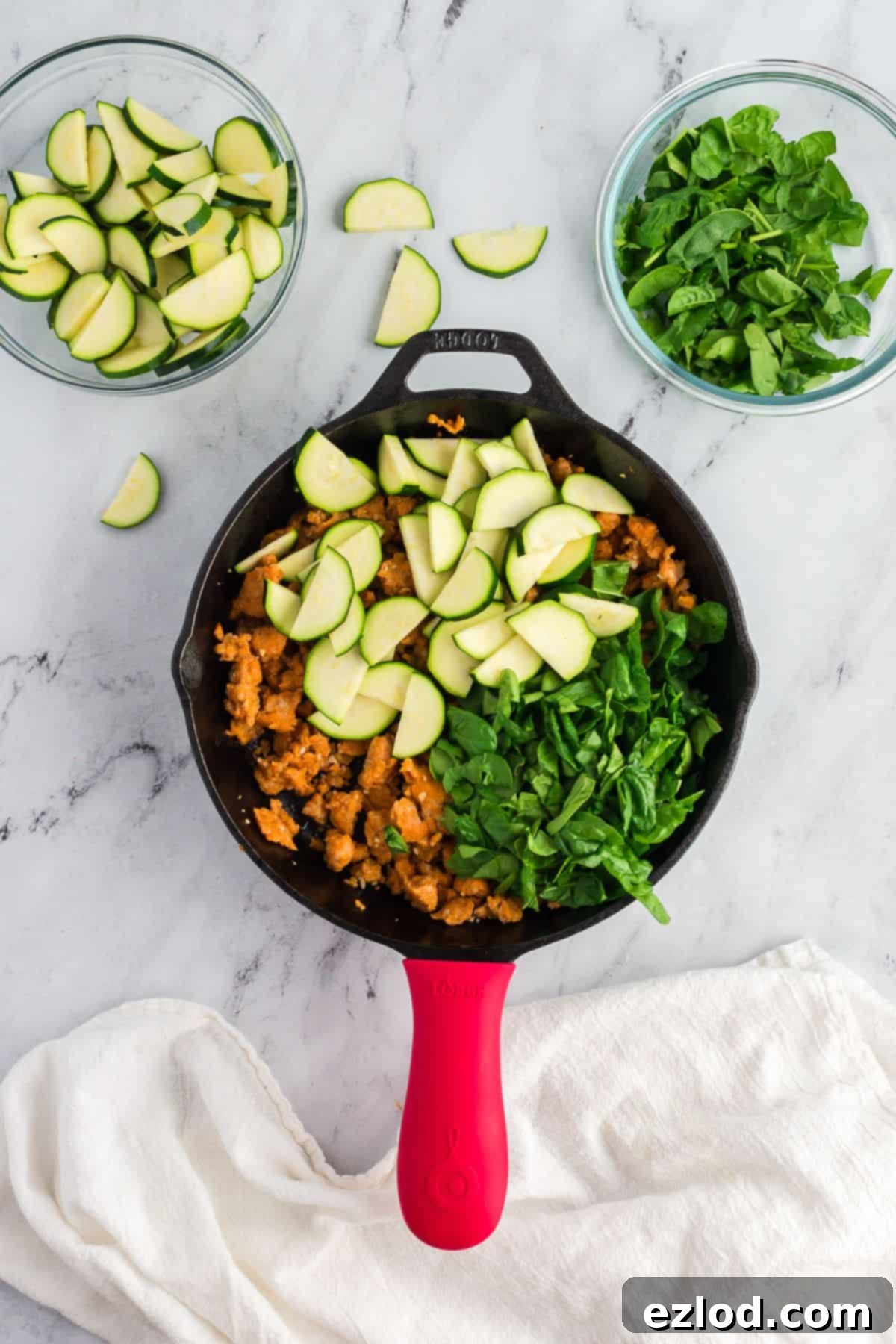 High Protein One Pan Zucchini Lasagna 6 A close-up view of a skillet showcasing browned ground chicken sausage mixed with tender, vibrant green zucchini slices and wilted spinach, creating the savory base for the zucchini lasagna.