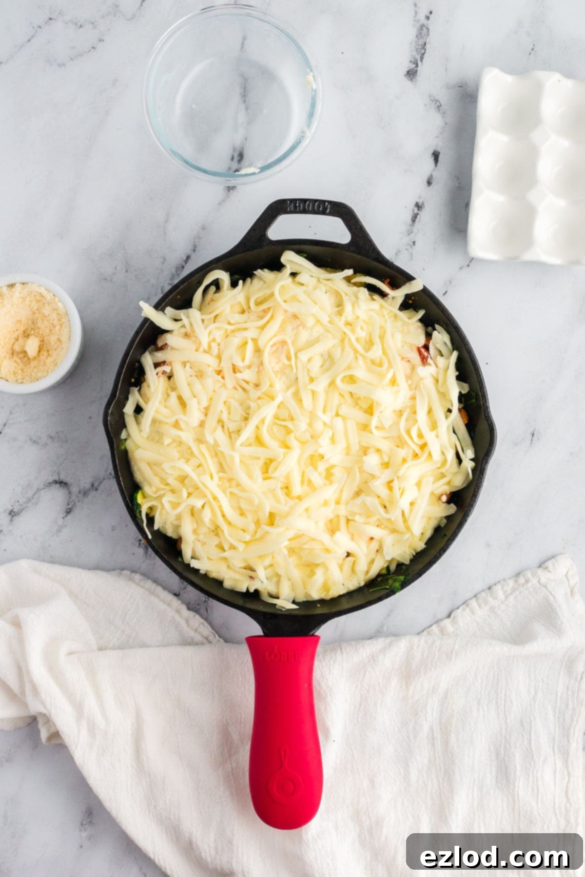 High Protein One Pan Zucchini Lasagna 8 A close-up of a skillet filled with layers of zucchini, sausage, and marinara, topped with creamy white ricotta cheese mixture and a generous amount of shredded mozzarella, ready for baking.