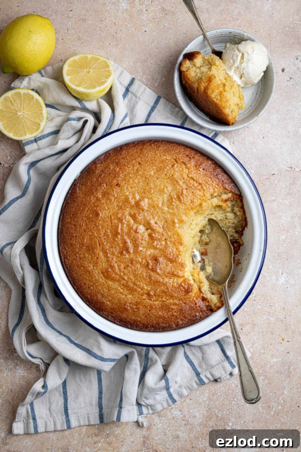 A beautifully presented vegan lemon elderflower almond pudding in a round baking dish, with a small serving in a bowl topped with ice cream, ready to be enjoyed.