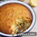 Close up of the pudding with a spoonful removed and sliced lemons in the background.