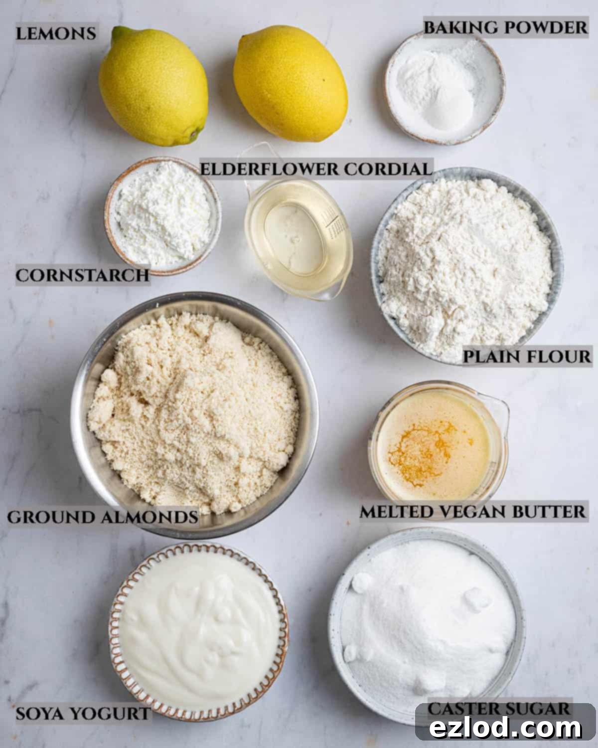 A collection of ingredients for lemon elderflower almond pudding, neatly arranged in bowls on a wooden surface, showing all components required.