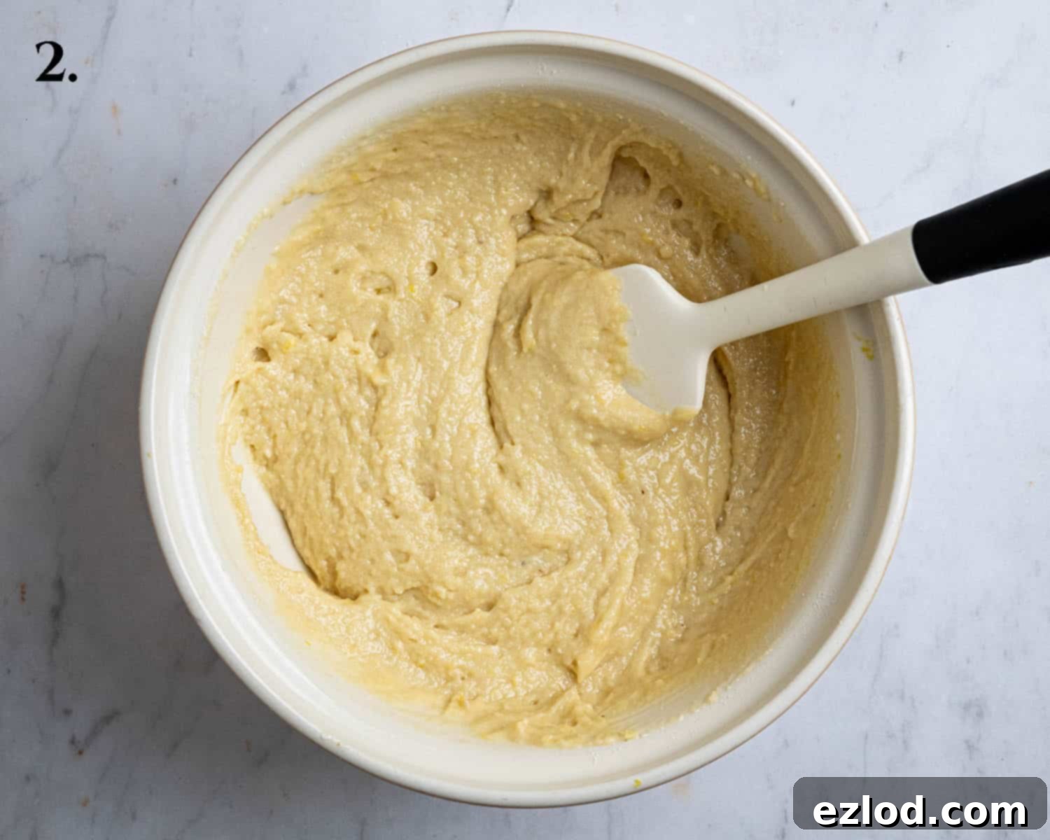 Step 2 of the recipe, showing the finished smooth batter for the lemon elderflower almond pudding, glistening in a mixing bowl.