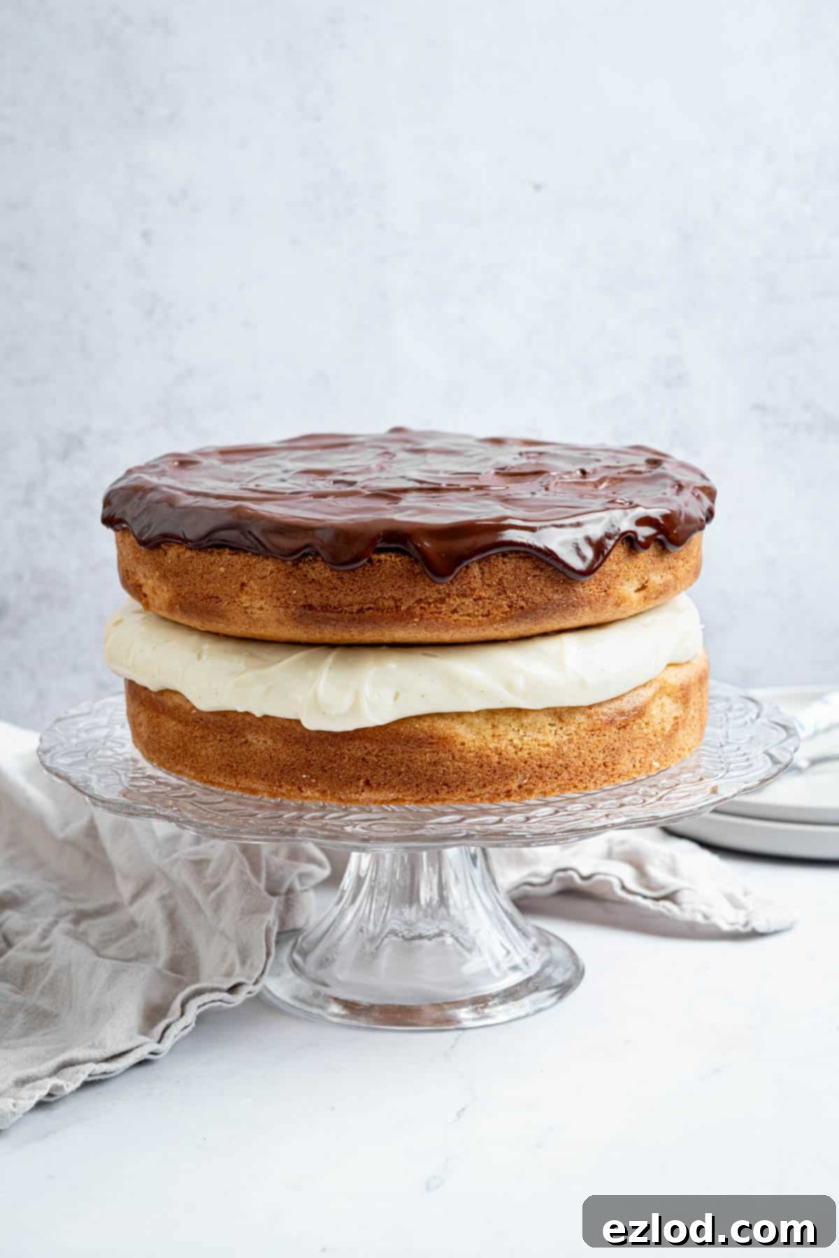 The fully assembled vegan Boston cream pie, glistening with chocolate ganache on a elegant glass cake stand, ready to be served.