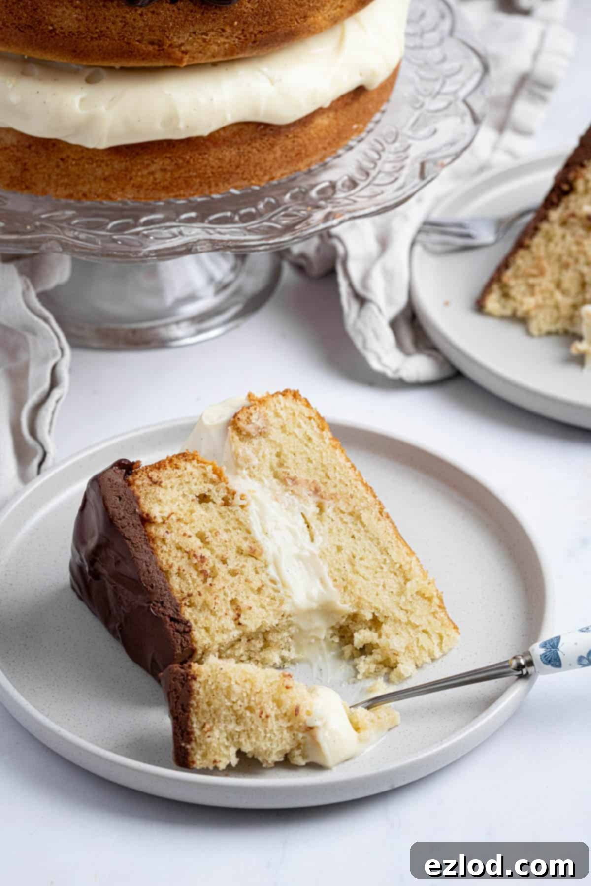 A perfect slice of vegan Boston cream pie on a plate, with a fork having removed a bite, emphasizing its delicious layers.