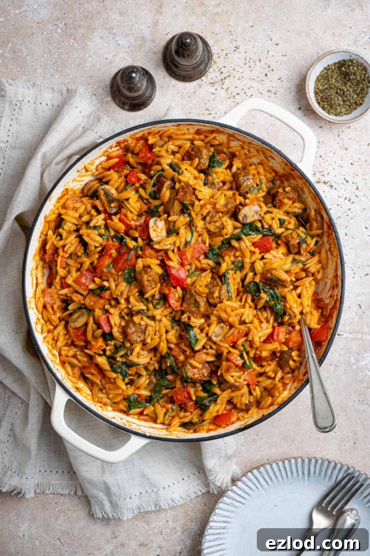 Spicy sausage orzo in a white pan, garnished with fresh herbs.