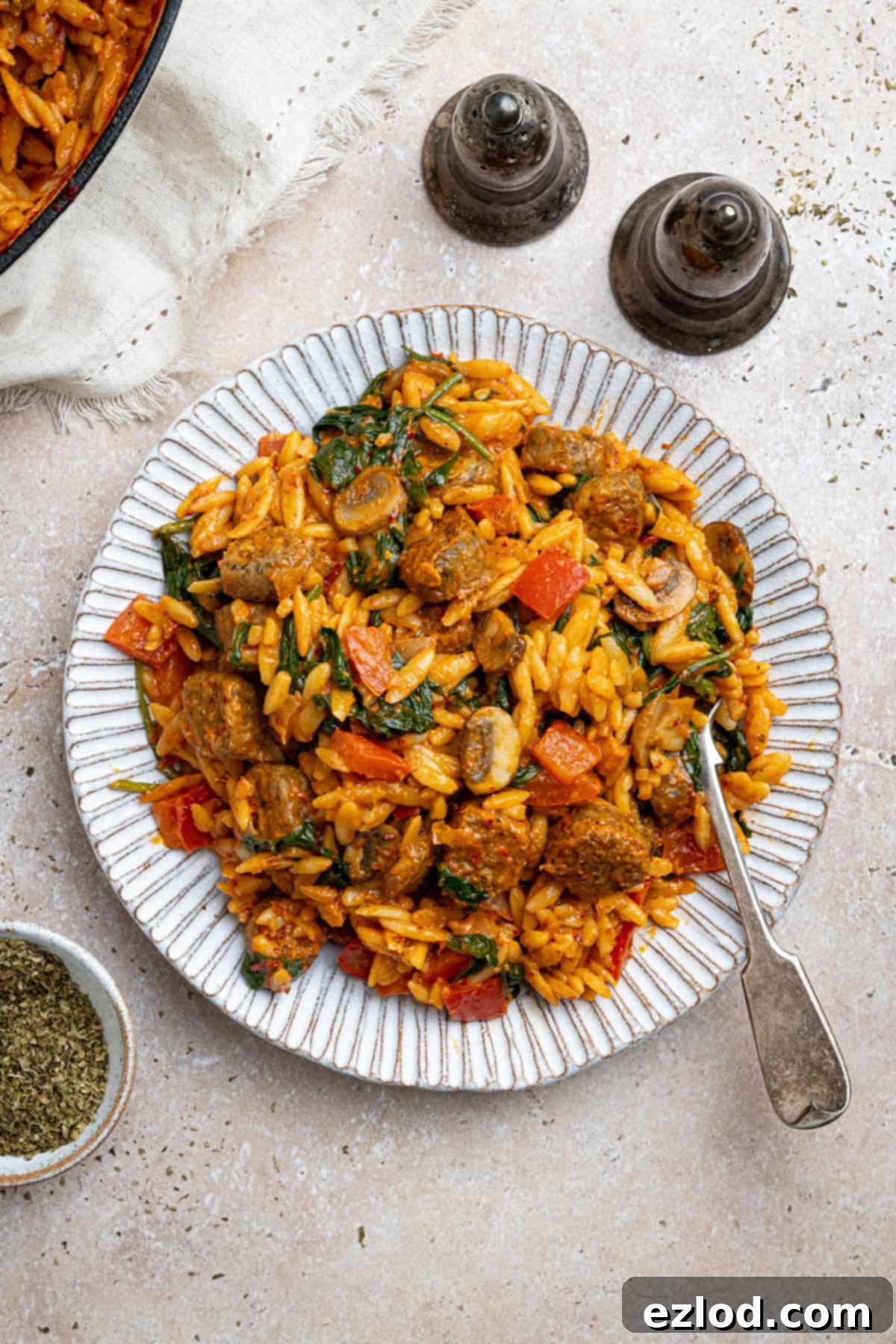 A serving of vegan spicy sausage orzo on a white plate, with salt and pepper shakers in the background.