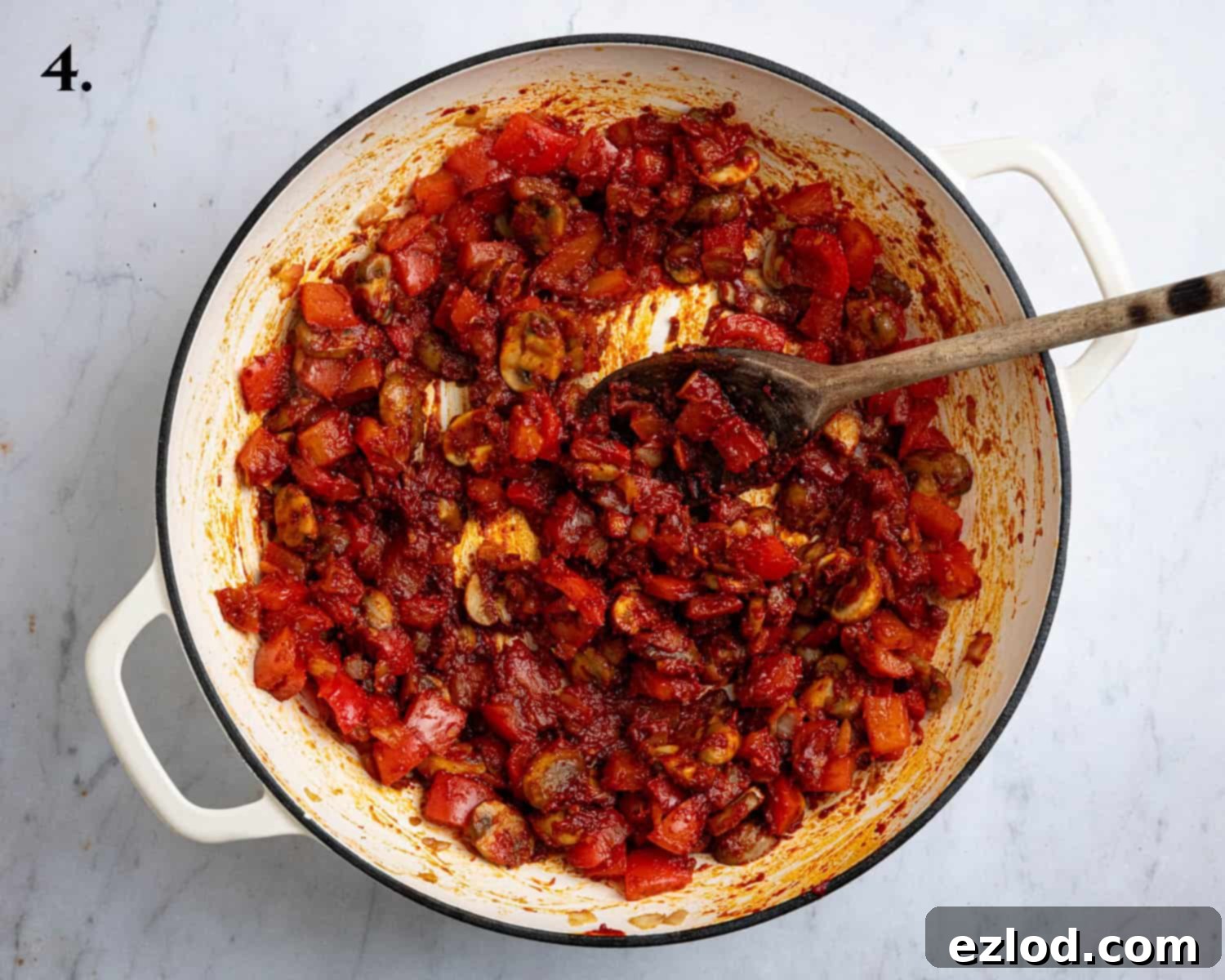 Step 4: Vegetables in a pan with added tomato paste and vegan 'nduja paste, being stirred.