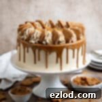 Vegan Biscoff cake on awhite cake stand with crushed cookies and a bowl of cookie butter.