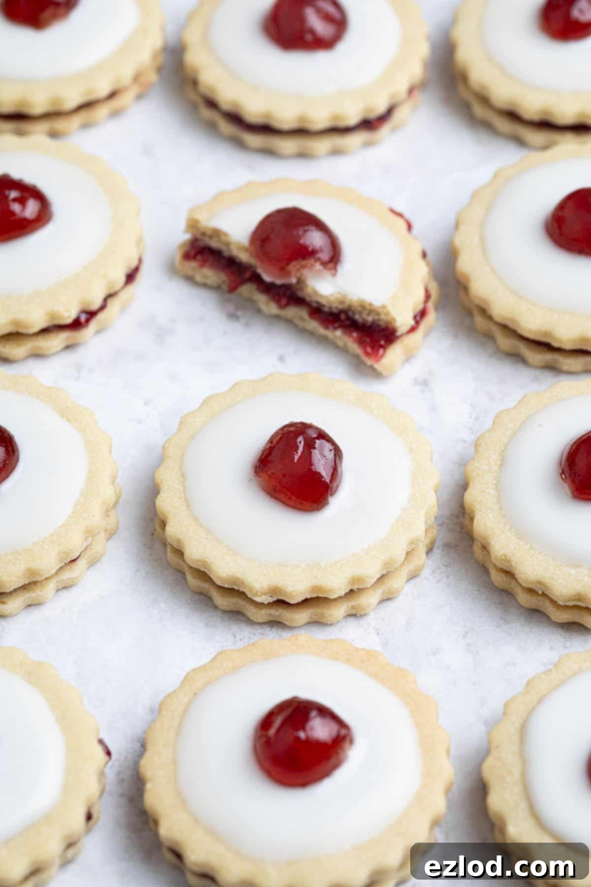 Rows of vegan empire biscuits on a white surface, one broken in half.