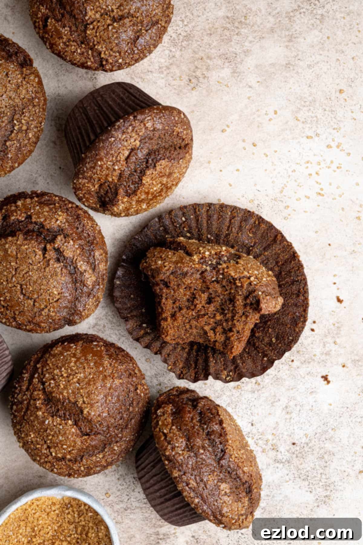 A vegan gingerbread muffin with a bite taken out, showing its soft interior, on a brown surface.