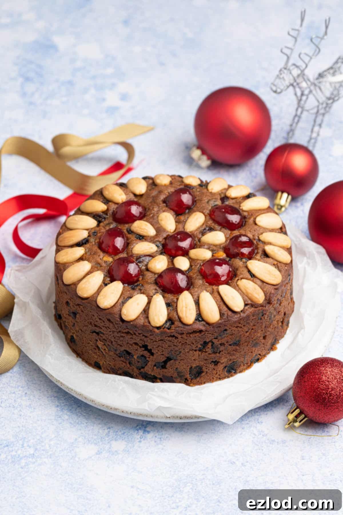 Small batch vegan Christmas cake on a plate surrounded by red baubles and ribbons.