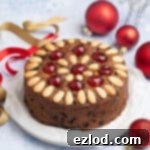 Small batch vegan Christmas cake on a plate surrounded by red baubles and ribbons.