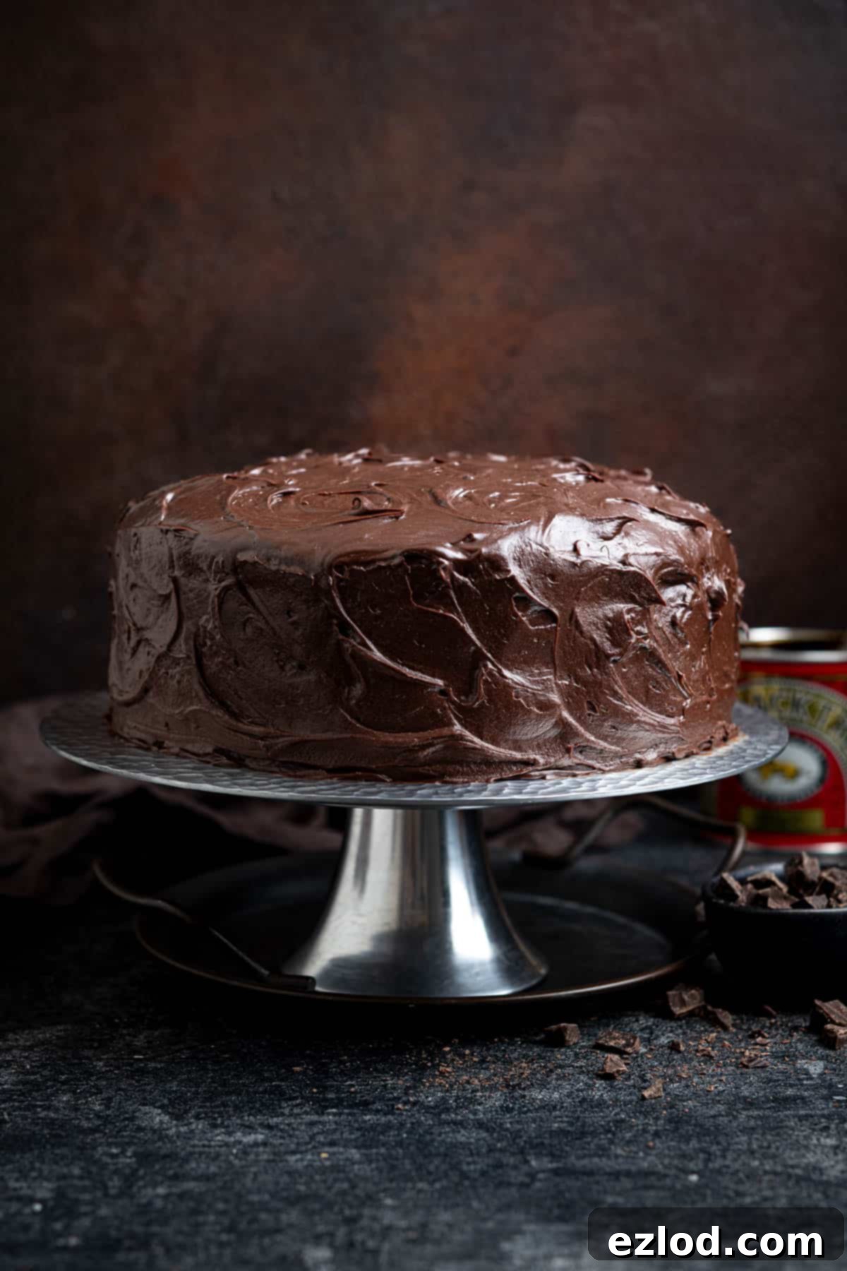 Decadent Vegan Treacle Chocolate Cake 2 Vegan treacle chocolate cake on a silver cake stand with a tin of treacle, showcasing its rich frosting and tempting appearance.