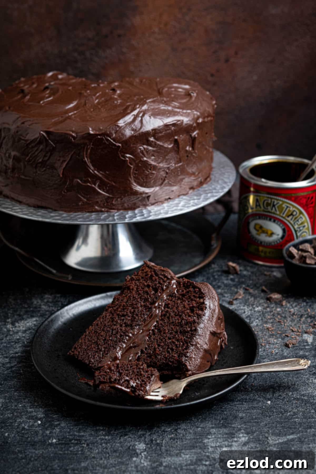 Decadent Vegan Treacle Chocolate Cake 12 A stunning arrangement of the treacle chocolate cake on a silver stand, with a slice on a black plate, and a tin of treacle.