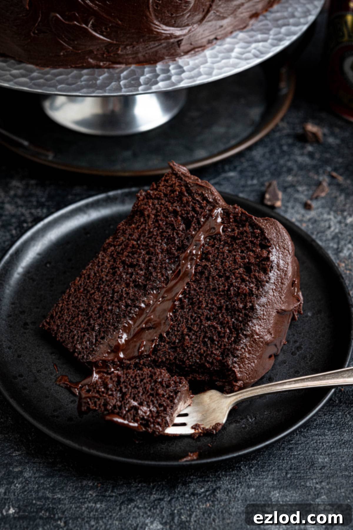 Decadent Vegan Treacle Chocolate Cake 3 A perfectly sliced piece of vegan treacle chocolate cake on a dark plate with a fork, highlighting its moist interior.