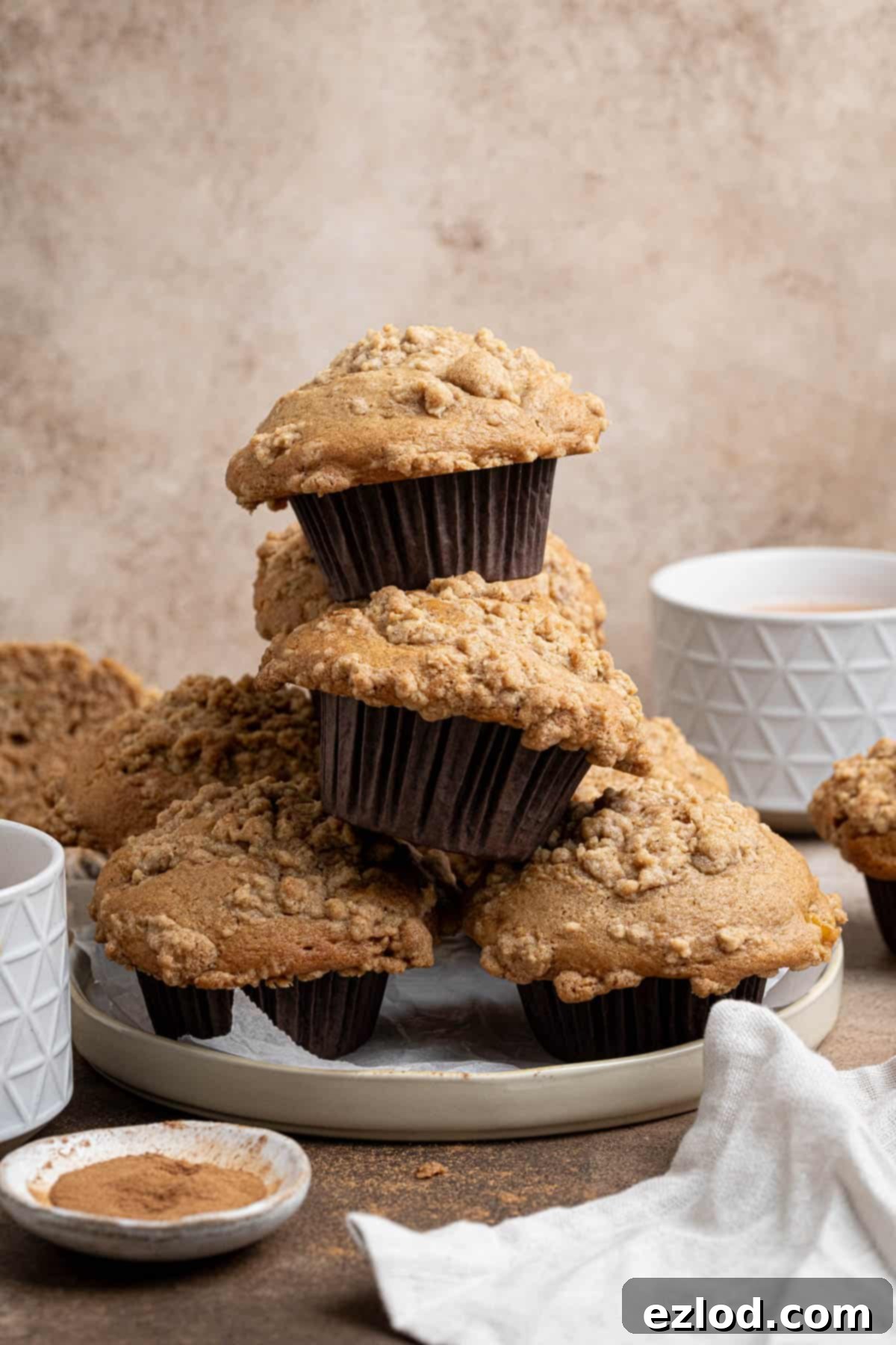 Spiced Pear Plant-Based Muffins 11 A charming stack of freshly baked vegan cinnamon pear muffins on a white plate, accompanied by two steaming cups of tea, creating a cozy autumn scene.