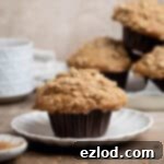Spiced Pear Plant-Based Muffins 13 A vegan cinnamon pear muffin on a plate with a stack of muffins and a cup of tea in the background.