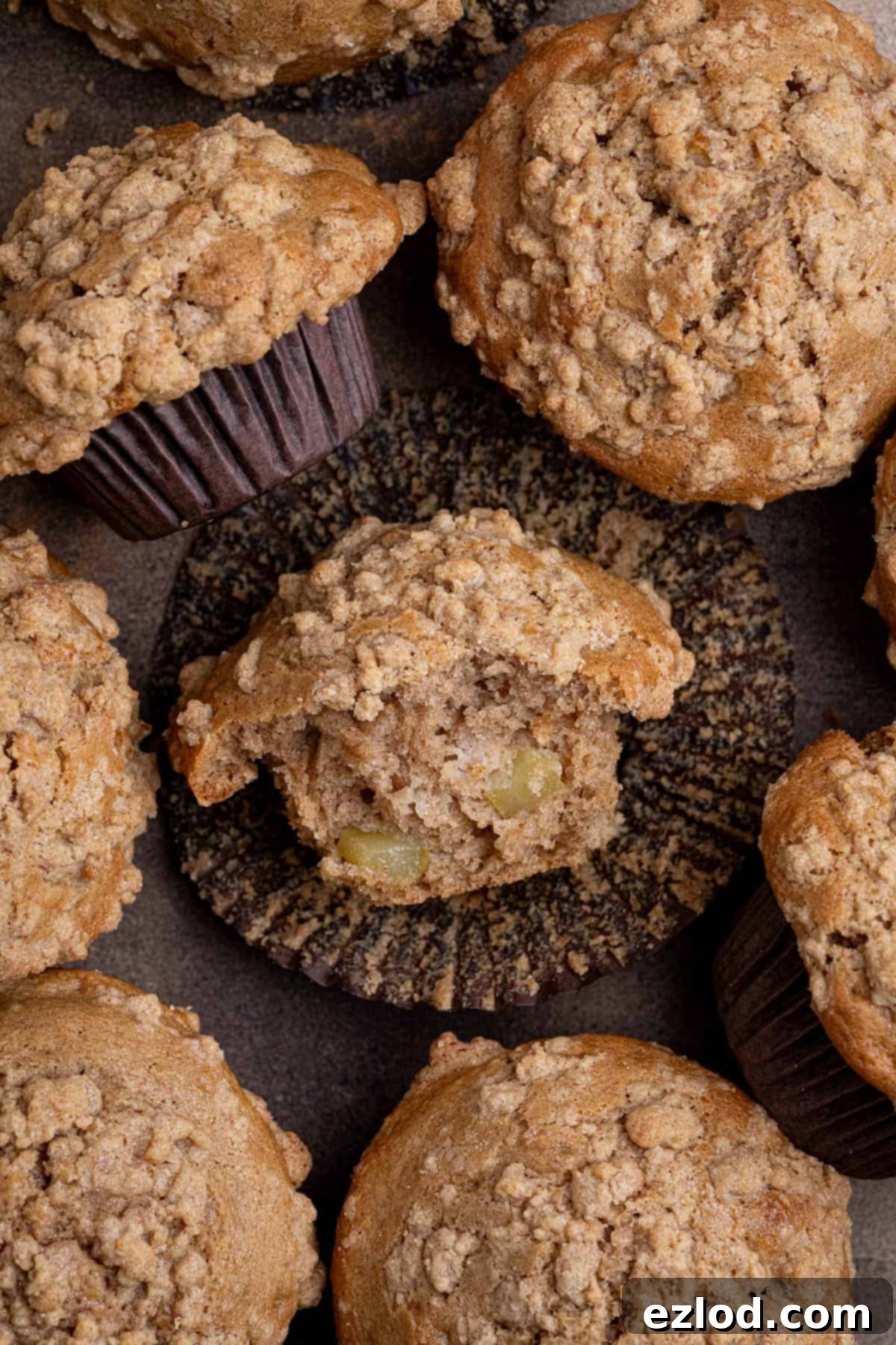 Spiced Pear Plant-Based Muffins 4 A close-up shot of several vegan cinnamon pear muffins, one with a bite taken out, showcasing the moist interior, pear chunks, and crumbly streusel topping.